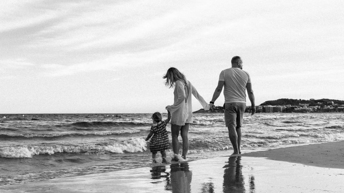 A family enjoys a peaceful walk along the beach with gentle waves.